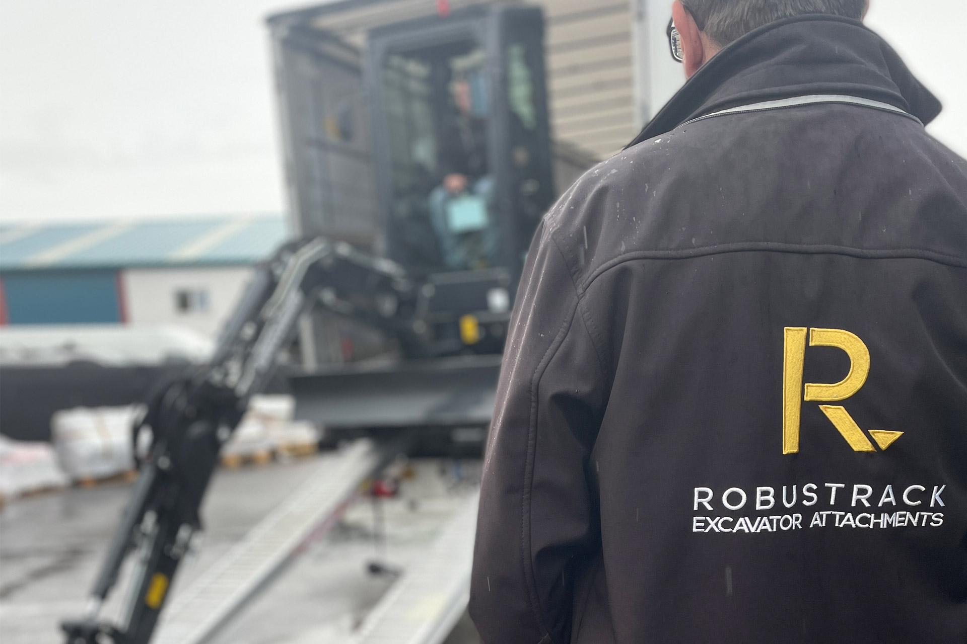 Robustrack staff watching the unloading of a black eurocomach digger