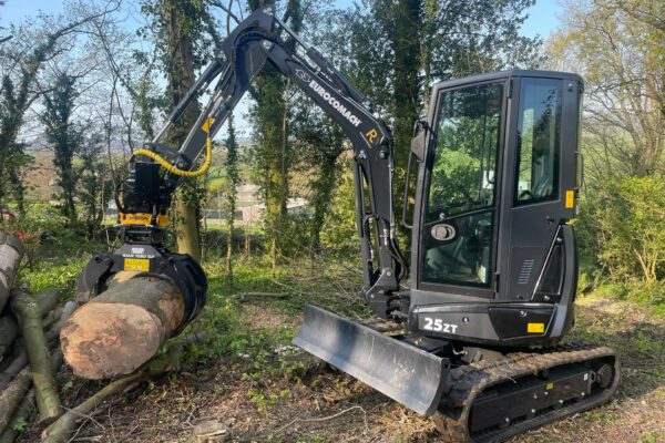 Black excavator with engcon tiltrotator and log grab attached with a tree trunk in the log grab.